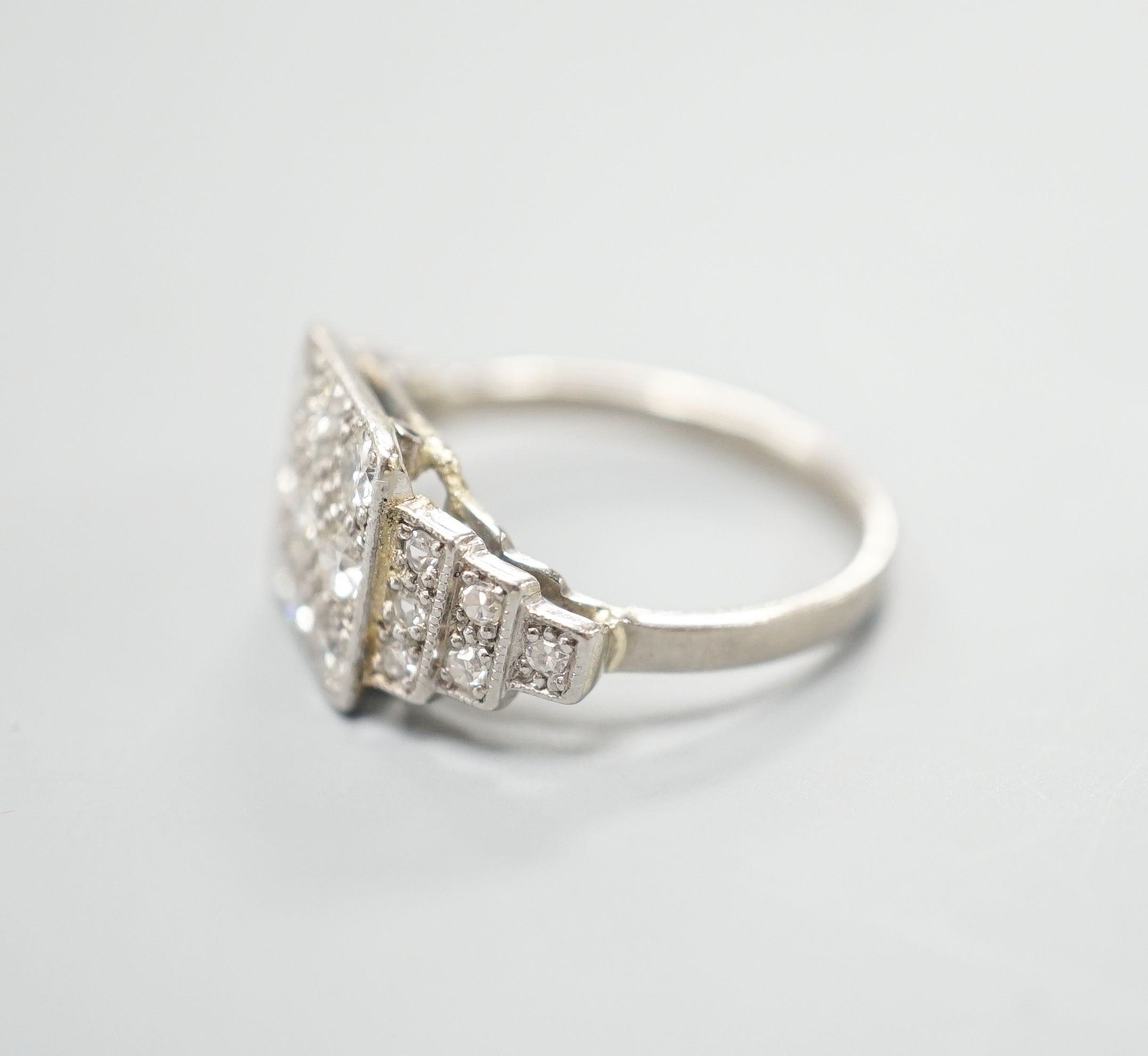 An Art Deco style white metal and nine stone diamond set tablet ring, with diamond set stepped shoulders, size K, gross weight 3.2 grams.